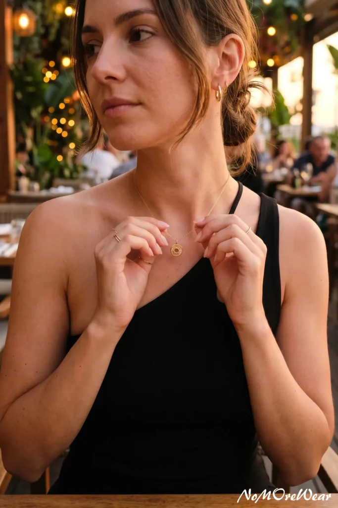 Detail shot of a woman's hands touching a gold necklace while wearing a modern one-shoulder asymmetrical tank top, featuring casual summer outfits for women.